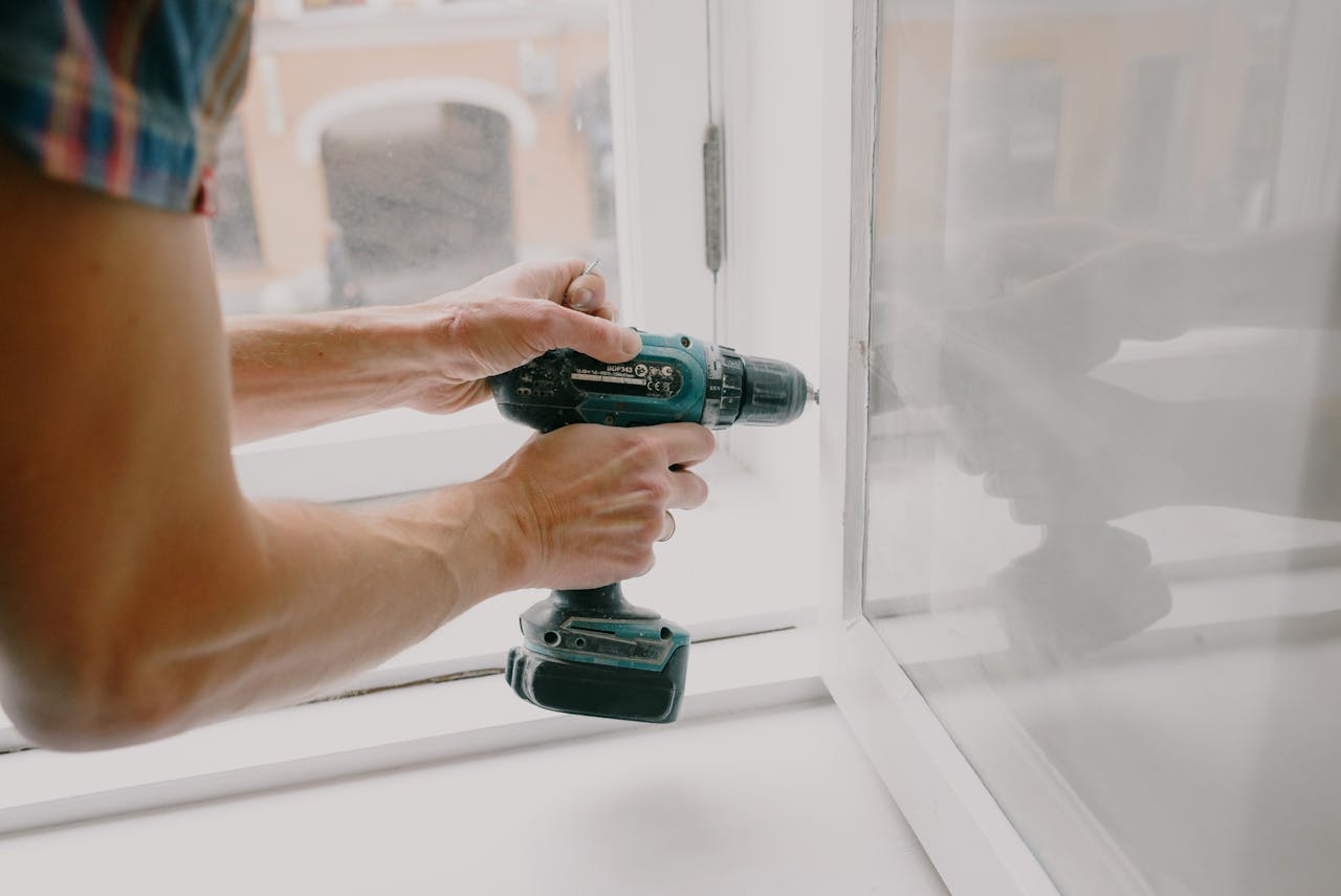 about-03 A person using an electric drill to repair or install a window indoors.